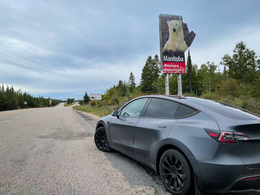 Tesla Model Y parked in front of the Welcome to Manitoba sign