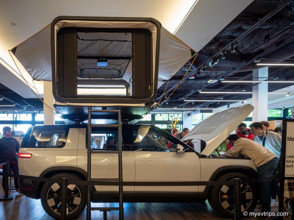 Rivian R2 display from the side with frunk open and tent topper