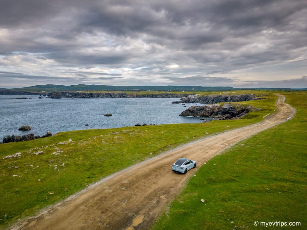 Tesla Model Y driving on a dirt road next to rugged coast line in Newfoundland