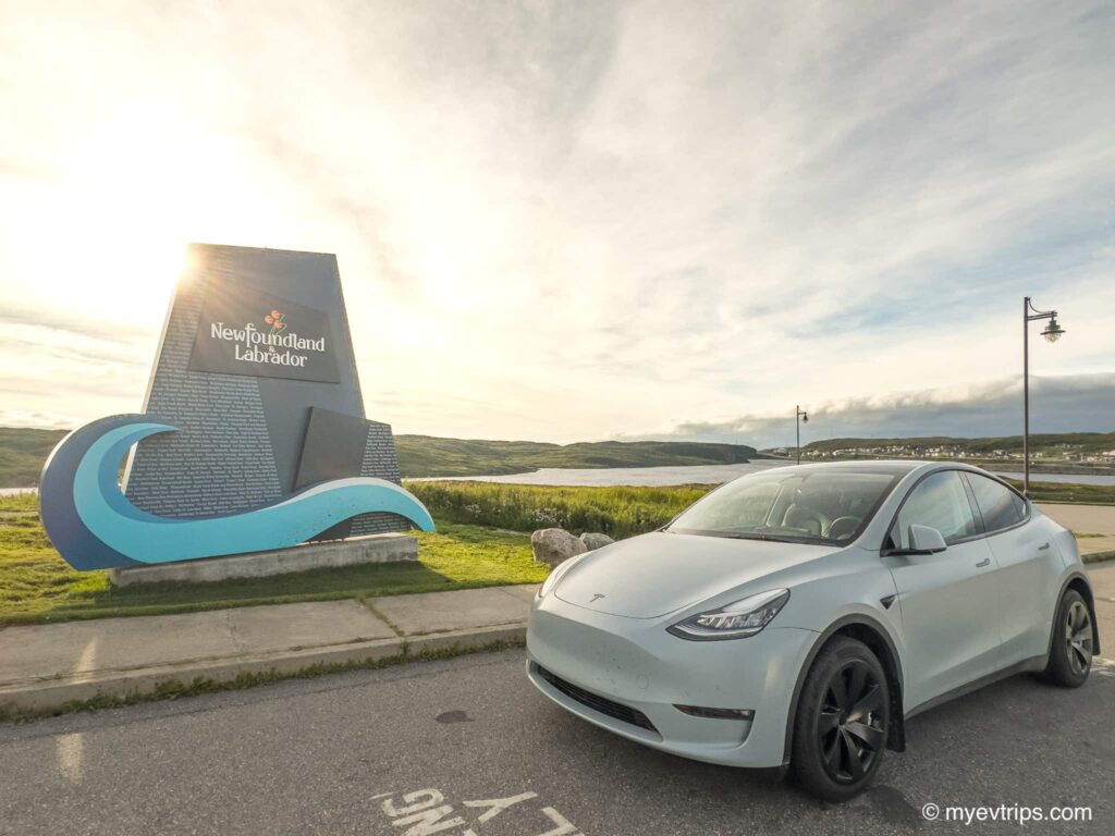 Tesla Model Y parked in from of the Newfoundland and Labrador sign in Port Aux Basque Newfoundland at sunrise