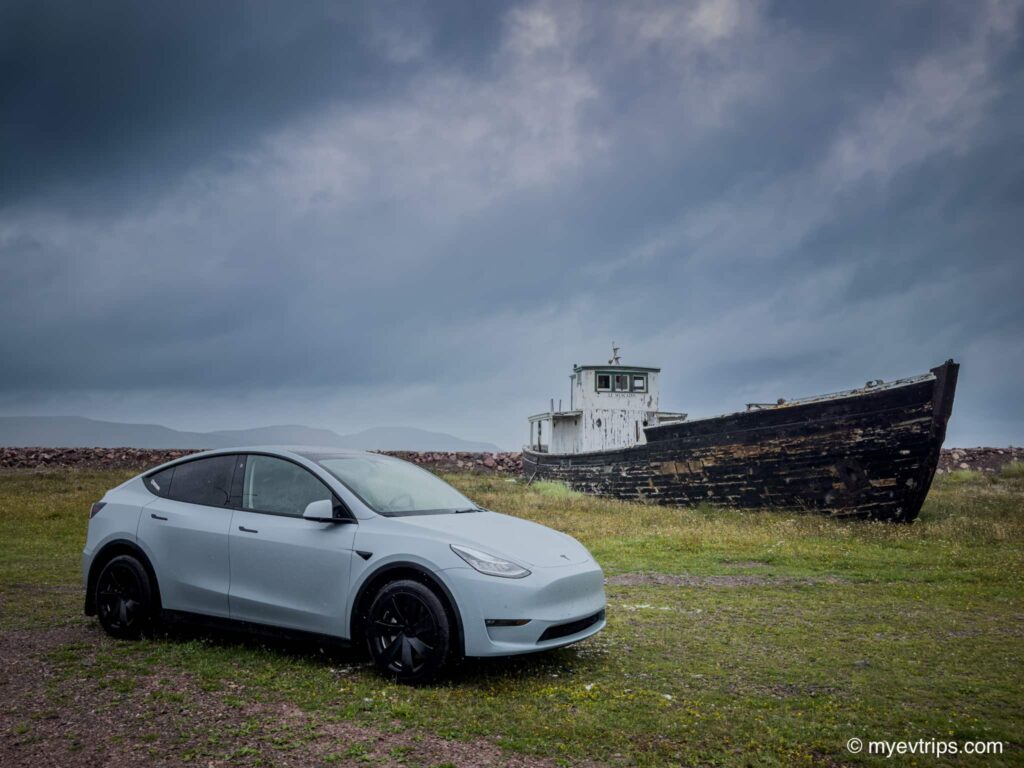 Tesla Model Y parked in front of an old grounded boat in Saint Pierre et Miquelon