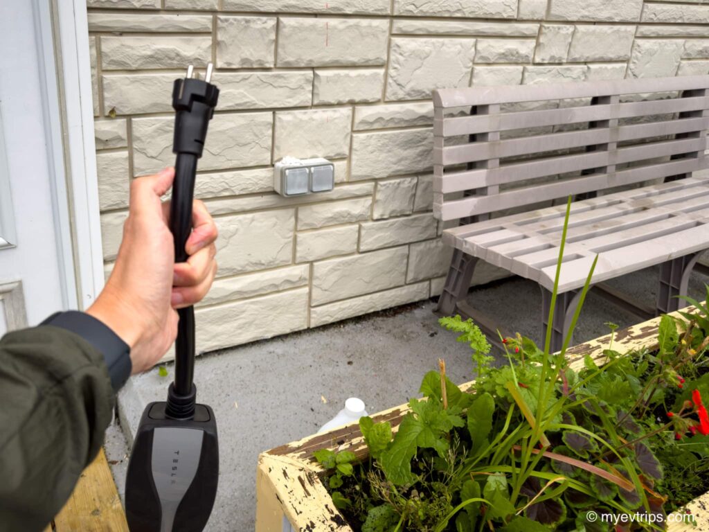 Saint Pierre EV charging - hand holding up Tesla mobile charger with Schuko adapter
