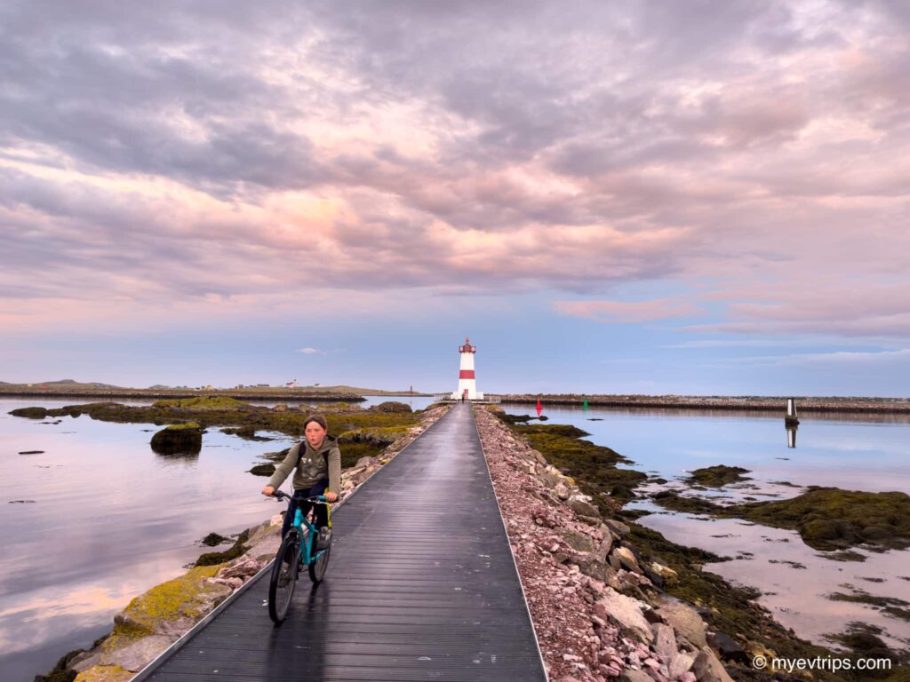 Boy on bike with Pointe aux Canons Lighthouse in distance at dusk