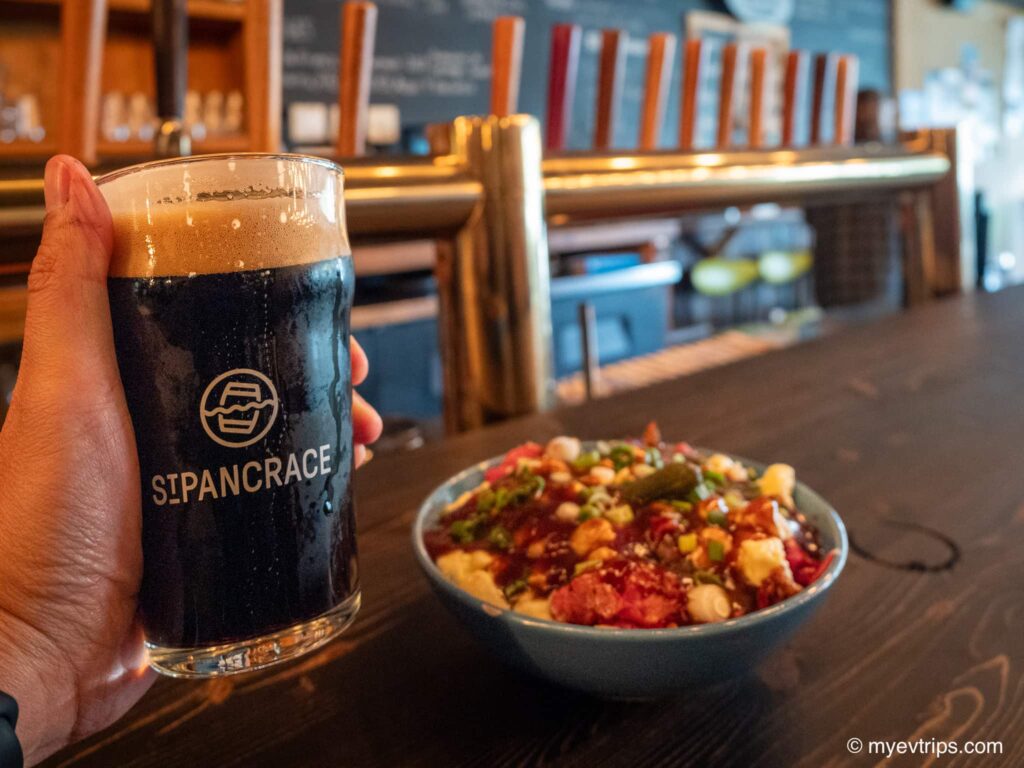 Hand holding up pint of dark beer at the Saint-Pancrace microbrewery in front of a plate of poutine.