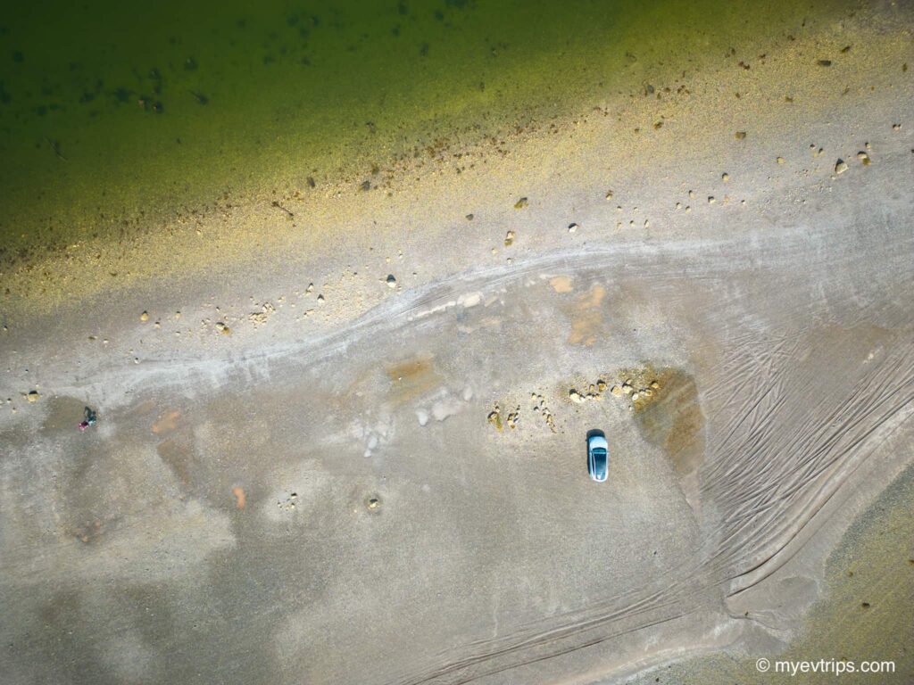 Aerial shot straight down of Tesla Model Y on the land bridge during low Ministers Island tides.