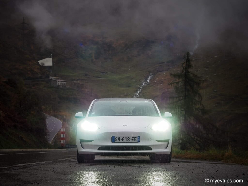 Tesla Model 3 parked in the rain with a waterfall in the background while on a Swiss Alps Road Trip